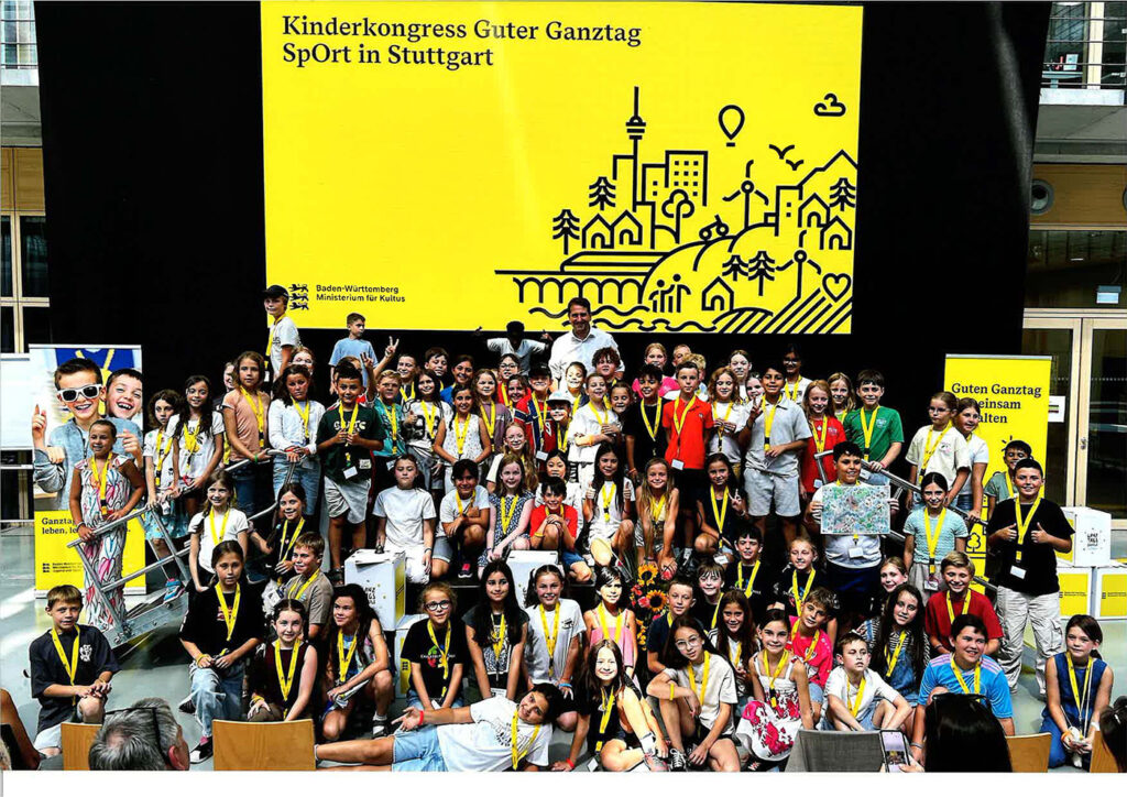 Kinder und Jugendliche beim Kinderkongress „Guter Ganztag – Sport in Stuttgart“ vor einer gelben Veranstaltungswand
