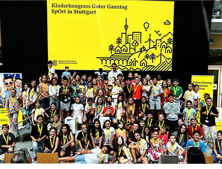 Kinder und Jugendliche beim Kinderkongress „Guter Ganztag – Sport in Stuttgart“ vor einer gelben Veranstaltungswand